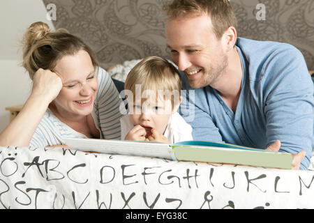 eine Familie auf dem Bett liegen und ein Buch zu lesen Stockfoto