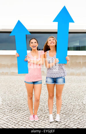 Zwei schöne und glückliche Mädchen hält einen riesigen blauen Pfeil Stockfoto