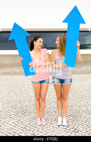 Zwei schöne und glückliche Mädchen hält einen riesigen blauen Pfeil Stockfoto