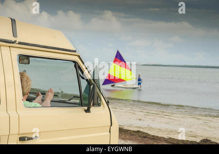 1981 Volkswagen Vanagon Westfalia am Strand von Dunedin Causeway, Florida. Beobachten ein Segelboot Sunfish. Stockfoto