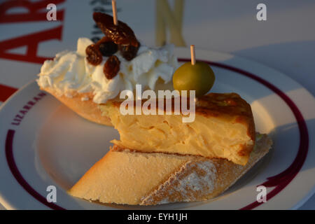 Pinchos Españoles bei Lizarran, Spanien. Im Vordergrund steht Tortilla & Olive, in den Hintergrund-Frischkäse, Rosinen und ein Datum. Stockfoto