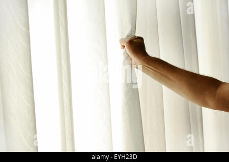 Die Hand eines Mannes ziehen ein Fenstervorhang für warme Tageslicht in den Raum zu betreten Stockfoto