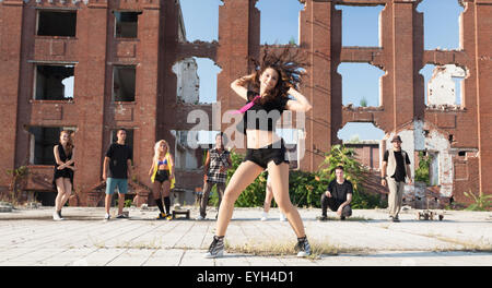 Young Girl Hip-Hop-Tanz in einem städtischen Platz mit ihren Freunden, die sie unterstützen. Natürliches Licht von der Sonne an Hochhäusern. Stockfoto