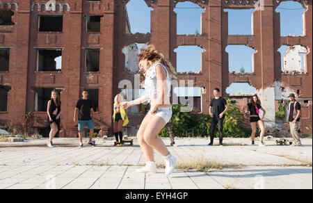 Junge Leute tanzen in einem städtischen Platz mit ihren Freunden im Hintergrund unterstützen. Natürliches Licht von der Sonne auf Hochhaus bauen Stockfoto