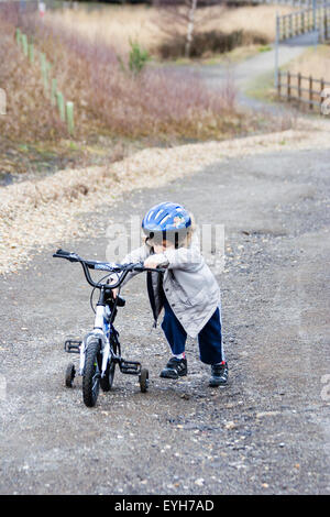 Jungen kämpfen Fahrrad mit Stabilisatoren, bis grobe Track im Winter zu drücken. Kaukasier Kind, 6-7 Jahre alt, mit Mantel und Helm. Stockfoto