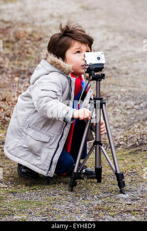 Kaukasier Kind, Junge, 6-7 Jahre alt. Im Freien im Winter in der Landschaft mit einer Kamera auf einem Stativ montiert, als er ein Foto. Stockfoto