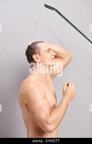 Vertikales Profil Schuss eines jungen Mannes, der unter der Dusche auf grauem Hintergrund Stockfoto