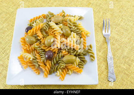 Farbige Makkaroni Nudeln Essen mit Oliven serviert auf die gelbe Tischdecke mit einer Gabel Stockfoto