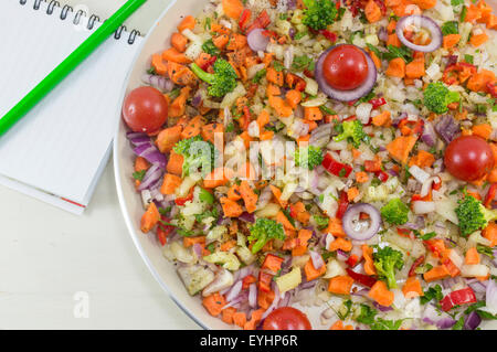 Salat auf einem Teller neben ein offenes Notizbuch und einen Stift für das Rezept schreiben. Zubereiten von Lebensmitteln Stockfoto