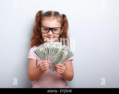 Glückliches Kind Mädchen in Gläsern, die Geld in die Hand und suchen mit Lächeln auf blauem Hintergrund mit leeren Textfreiraum Stockfoto