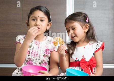 Zwei niedliche indische Mädchen essen. Asiatische Geschwister oder Kinder freuen sich über traditionelle snack Murukku, Lebensstil zu Hause. Stockfoto