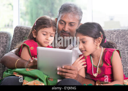 Moderne Technologie-Konzept. Indische Familie zu Hause. Asiatischen Vater und Kinder mit Touchscreen-Tablet-Computer, auf dem Sofa sitzen, Stockfoto