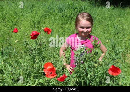 Mädchen stehen in das Beet mit blühenden roten Mohnblumen Stockfoto