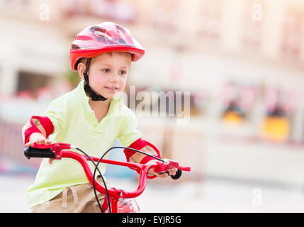 Kleiner Junge spielt im Freien, niedliches fröhliches Kind Spaß im Sommer-Camp, netter junge Reiten auf roten stilvolle Fahrrad Stockfoto