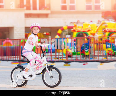 Fröhliches kleines Mädchen reiten auf dem Fahrrad im Vergnügungspark, glückliche unbeschwerte Kindheit, Spaß im Freien im Sommer-Camp Stockfoto