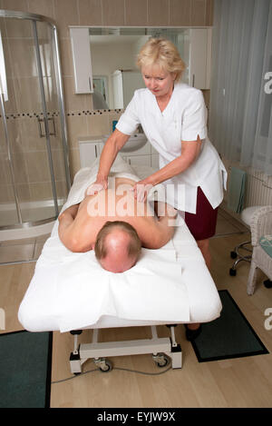 Masseurin arbeitet mit einem männlichen Klienten mit einer entspannenden Rückenmassage Stockfoto