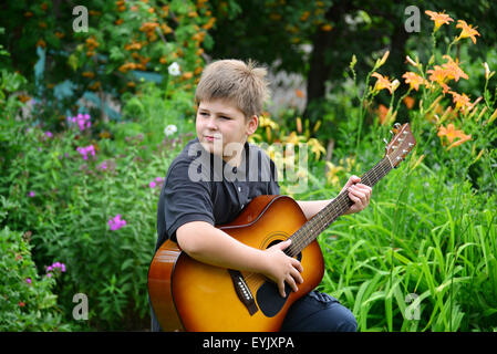 Teenboy spielt Gitarre im Freien im Sommer Stockfoto