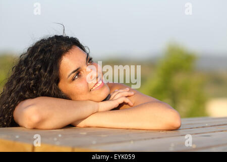 Ehrliche Mädchen denken und auf der Suche nach seitwärts entspannend in einem Park bei Sonnenuntergang mit dem Himmel im Hintergrund Stockfoto