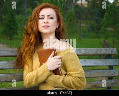 Ingwer-kurzhaarige Frau sitzen auf einer Bank mit Buch im park Stockfoto