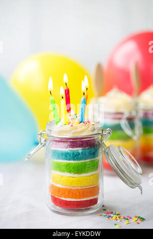 Regenbogen-Schicht-Kuchen im Glas mit Geburtstagskerzen Stockfoto