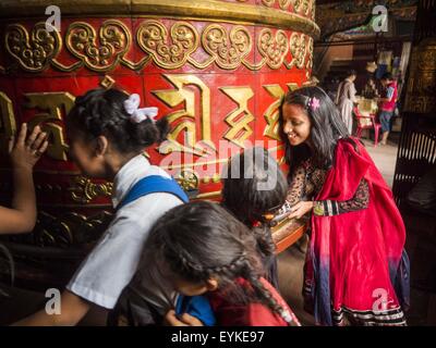 31. Juli 2015 spin - Kathmandu, Nepal - Schülerinnen und Schüler eine Gebetsmühle in einem tibetischen Kloster in der Nähe von Bodhnath Stupa. Bodhnath Stupa im Abschnitt Bouda Kathmandu gehört zu den am meisten verehrten und ältesten buddhistischen Stupas in Nepal. Das Gebiet ist als Zentrum der die tibetische Flüchtlingsgemeinschaft in Kathmandu entstanden. Bei Vollmond Nächte Tausende von nepalesischen und tibetischen Buddhisten kommen zur Stupa und Prozessionen rund um den Stupa beteiligen. Die Stupa wurde schwer beschädigt, in dem Erdbeben von 25. April 2015 und Menschen dürfen nicht mehr auf der Stupa, Klettern, jetzt sind sie Fuß den Fuß und beten w Stockfoto