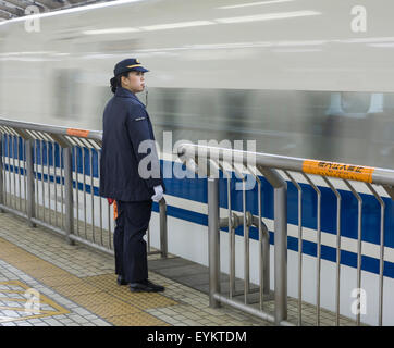 Frau Bahnhof Wache steht auf Plattform wie ein Hochgeschwindigkeitszug vom Bahnhof Tokio in einer Unschärfe fährt. Stockfoto