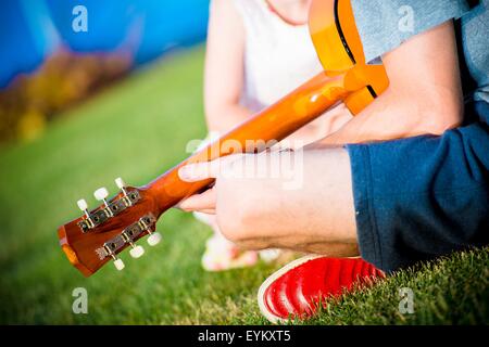 Papa, Gitarre zu spielen, für seine Tochter beim Sitzen auf dem Hinterhof-Rasen. Hinterhof Fun Time. Stockfoto