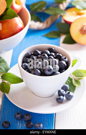 Frische Heidelbeeren in eine weiße Tasse auf farbigen Hintergrund Stockfoto