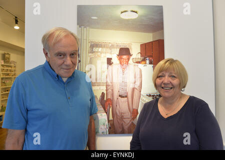 Huntington, New York, USA. 1. August 2015. GEORGE CARRANO und LOIS YOUMANS stellen durch ein Foto von Margaret Wells von einem senior Mann gekleidet zur Kirche, an der Rezeption für Projekt lebt Ausstellung in der Fotofoto Gallery. Mehr als 200 Einwohner im ganzen 15 New York städtische Wohnprojekte erhielten Einwegkameras Film zu fotografieren, was sie in ihrer Welt wichtig ist. Das Fotoprojekt entstand durch Carrano und das Buch, das Projekt lebt von Carrano, C. Davis und J. Fisher, mit alle Einnahmen aus dem Verkauf an residente Programme in New York City Housing Authority gespendet werden bearbeitet wurde. Stockfoto