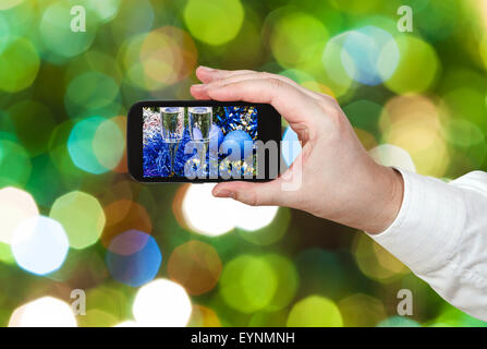 Mann nimmt Foto von Weihnachten Stillleben - zwei Gläser Champagner mit blauen Xmas Kugeln und Lametta auf verschwommene grüne Weihnachten-tr Stockfoto