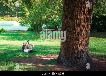 Mann liest Buch, ein junger Mann liest ein Buch an einem Sommernachmittag im Park der Villa Borghese, Rom, Italien. Stockfoto