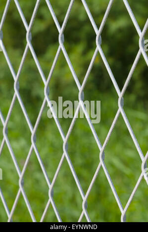 Defokussierten metallischen Volumennetz Zaun vor grünem Hintergrund Stockfoto