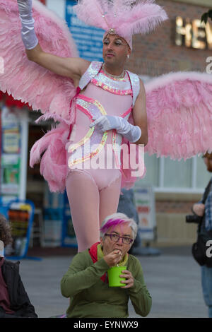 Stockton, UK, Samstag, 1. August 2015. Eine sitzende Frau in Stockton High Street hat ein al Fresco Essen, nichts von einem männlichen Straßenkünstler stehen hinter ihr, verkleidet als Rosa Engel. Die Straßenkünstler nimmt an Instant Light, 28. Stockton International Riverside Festival teil. Stockfoto