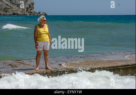 Senior ältere Dame steht auf der Strand-Leiste auf Hintergrund der Wellen planschen. Stockfoto