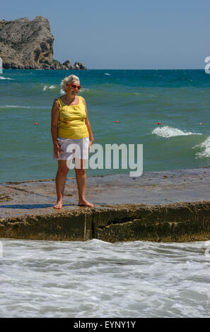Senior ältere Dame steht auf der Strand-Leiste auf Hintergrund der Wellen planschen. Stockfoto