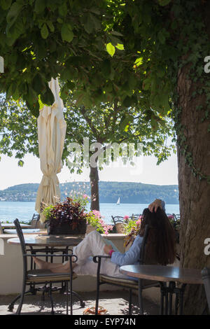 Eine junge Frau, die ein Buch im Schatten in ein Café-Restaurant am Ufer eines Sees Stockfoto
