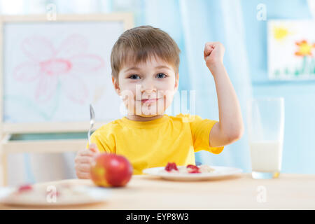 Kind isst gesundes Essen zeigt seine Stärke im Innenbereich Stockfoto