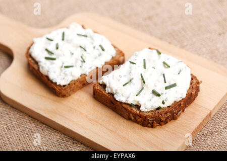 Zwei Scheiben würzigen Butterbrot mit grünen Zwiebeln obendrauf auf Holzbrett Stockfoto