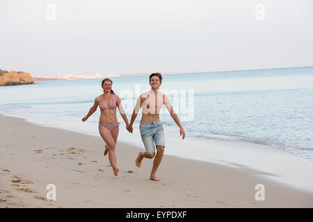 Glückliches junges Paar laufen und halten die Hände an einem Strand Stockfoto