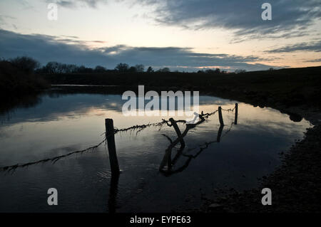 Stacheldraht auf einen Zaun, der durch Wasser aus einem Fluss bei Sonnenuntergang an einem Wintertag verschlungen worden Stockfoto