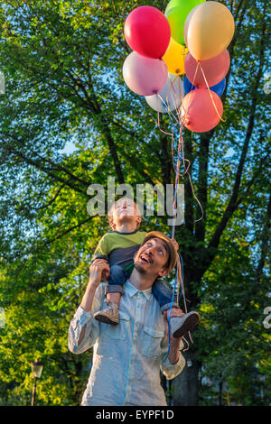 Vater und Sohn zu Fuß in den Park mit Luftballons an einem Sommerabend Stockfoto