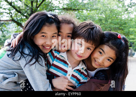 Reihe von vier lächelnden Kinder, 7-9 Jahre alt, Kopf und Schultern, Gesichter der Betrachter mit Blickkontakt. 3 japanische Mädchen und einen Kaukasischen Jungen. Umarmen sich. Stockfoto