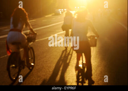 Verschwommenes Foto von Frauen auf dem Fahrrad fahren in der Stadt bei Sonnenuntergang in schönes Licht Stockfoto