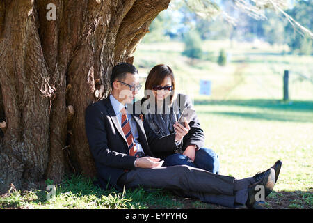 Paar sitzt unter Baum betrachten Telefon Stockfoto