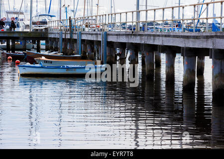 Kleine Fischerboote vor Anker in einer Marina mit einem Steg und Leute Angeln im Hintergrund. Stockfoto