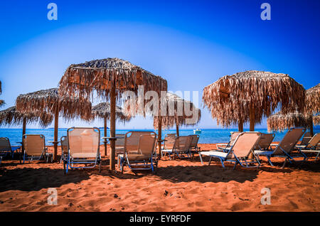 Stroh-Sonnenschirmen und liegen an einem Sandstrand in Griechenland. Sonnenschirme und Solarium am Strand. Stockfoto