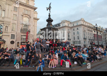 Touristen sitzen auf den Stufen der Shaftesbury-Gedenkbrunnen und Statue des Eros, Piccadilly Circus, London, England, UK Stockfoto