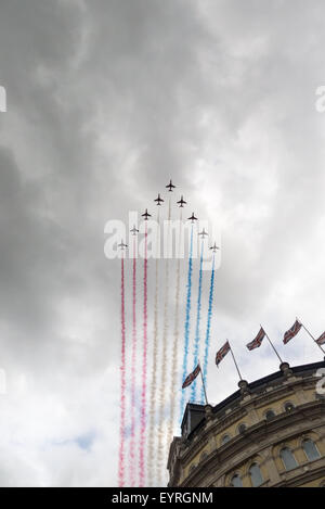 Trafalgar Square in London, Wettsektor. Die Red Arrows fliegen vorbei Streaming-rot, weiß und blau über ein Gebäude mit Union Jack-Flaggen. Stockfoto