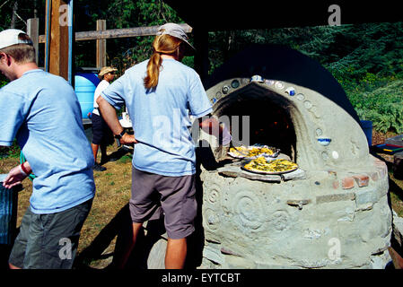 Arbeitet Man mit einem langen Pferdeschwanz Knoblauch Brotbacken im Outdoor Holz Cob Backofen auf Knoblauch-Festival Stockfoto