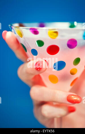 Zarte Frauenhand mit bunt bemalten Finger Nägel halten einen bunten und festlichsten Cocktail / Martini-Glas Stockfoto